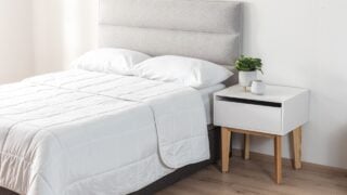 Bright bedroom with textured light gray upholstered headboard, crisp white bedding and modern white nightstand with natural wood legs, styled with minimalist decor and soft morning sunlight ambiance.