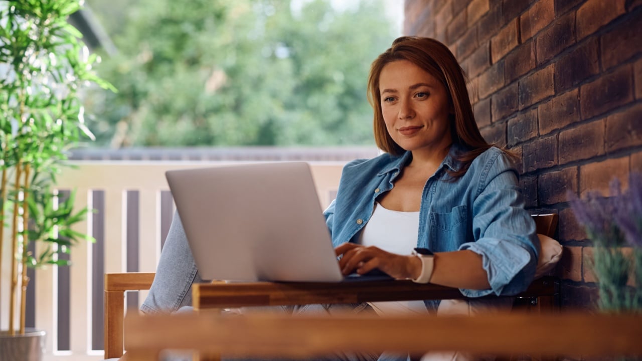 Smiling woman using laptop while relaxing on the porch. Copy space.