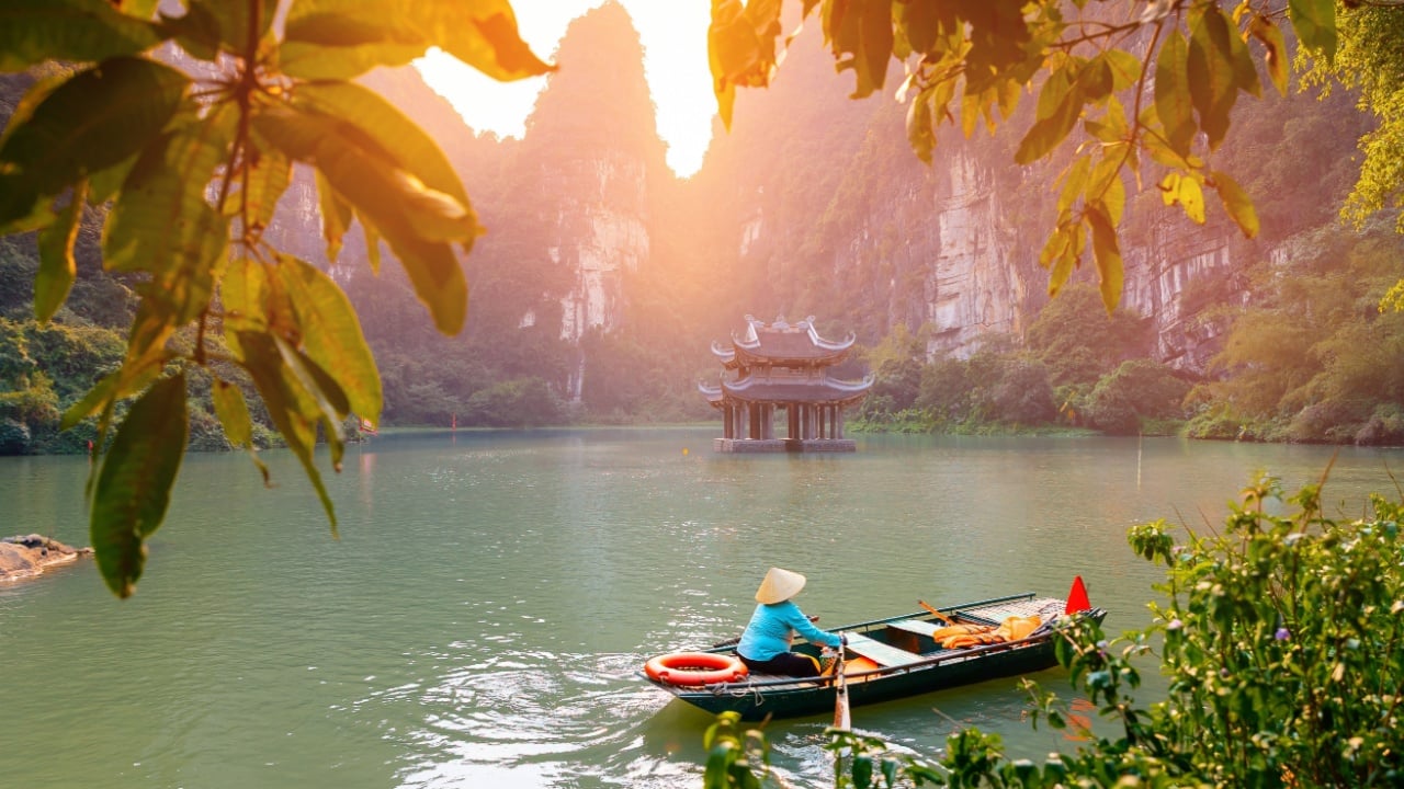 Scenic landscape of Ninh Binh with boat on river and ancient pagoda at sunset in Tam Coc National Park.