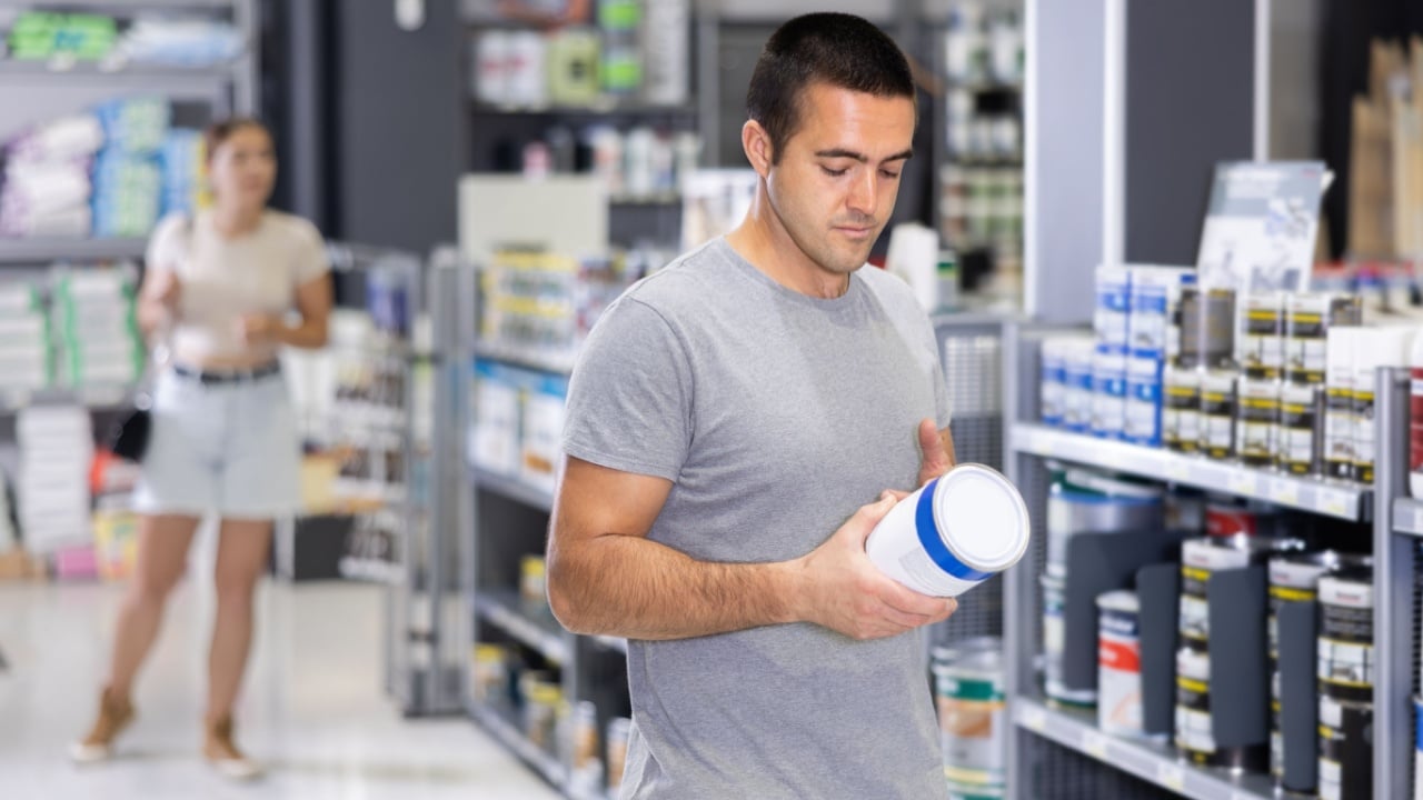 Man chooses and buys can of paint at a hardware shop