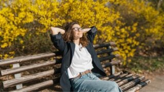 Relaxed young curly woman in glasses enjoying spring sun on a city bench