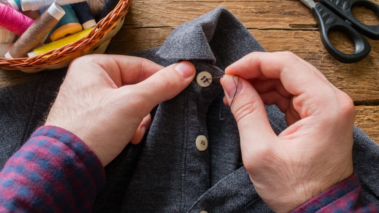 man sews a button to his shirt