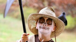 A young child is dressed in a scary Scarecrow halloween costume on a fall day.