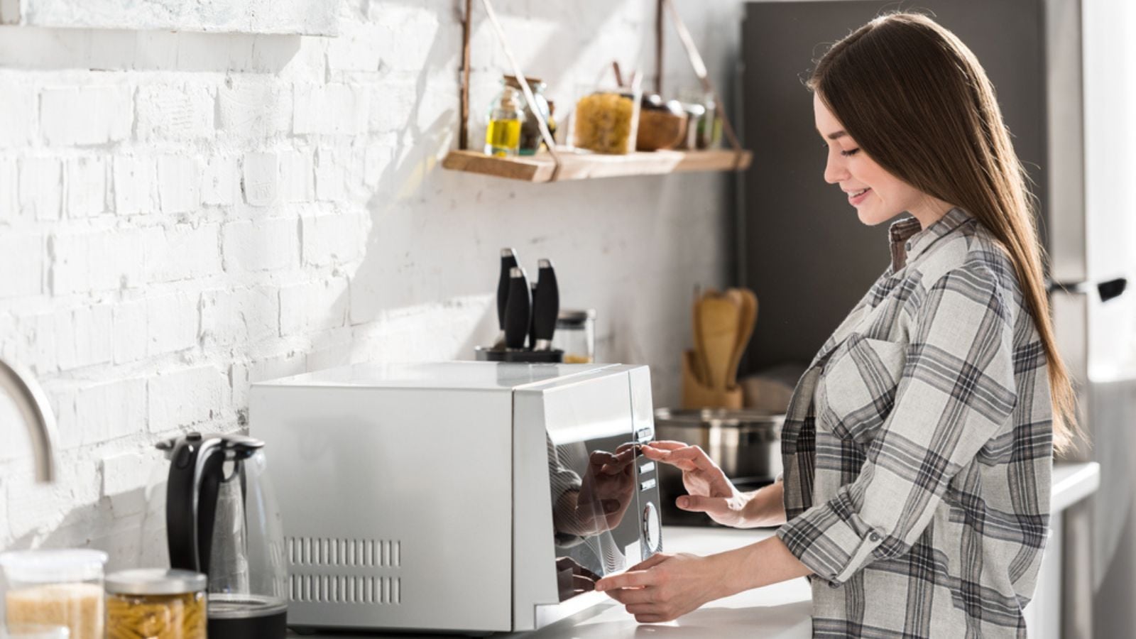 Side view of smiling woman in shirt using microwave in kitchen