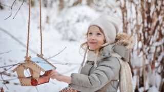 a little girl fills a bird feeder in winter
