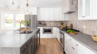A white kitchen detail with stone countertops, gold light fixtures above the island, and a brown tiled backsplash. No brands or logos.
