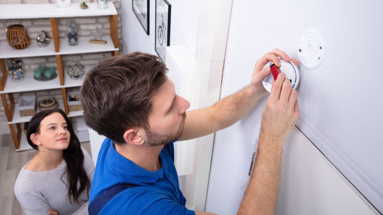 Happy Woman Standing Near Serviceman Replacing Battery In Smoke Alarm, Carbon Monoxide Alarms