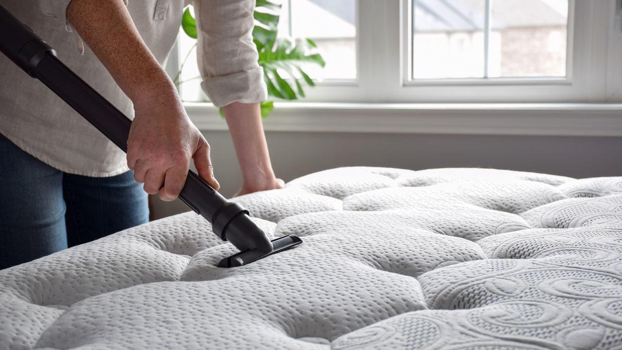 Woman using vacuum cleaner to vacuum mattress in a bedroom