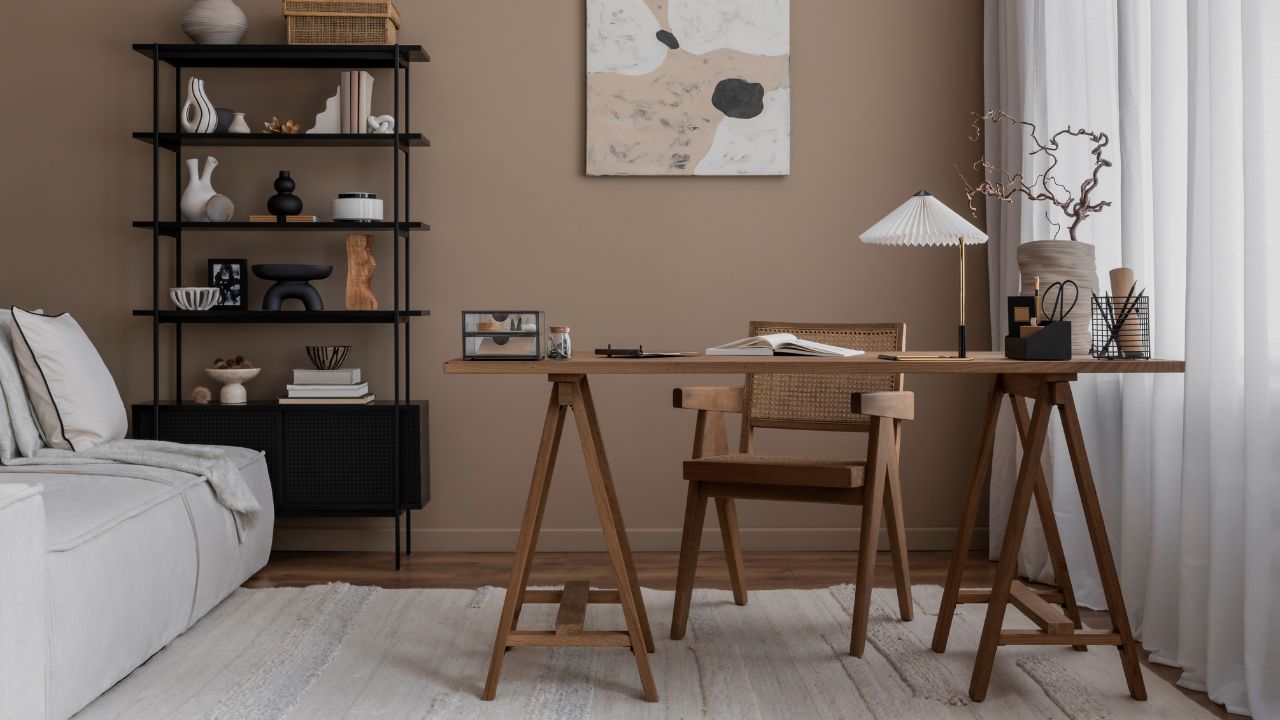Creative composition of warm and cozy workspace interior with mock up poster frame, wooden desk, modular sofa, black rack, rattan chair, stylish lamp and personal accessories. Home decor.