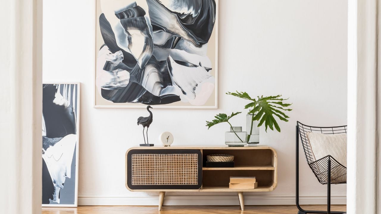 Modern design home interior of living room with wooden commode, design black armchair, tropical leafs and elegant accessories. Stylish home decor. Mock up abstract paintings on the wall. Template