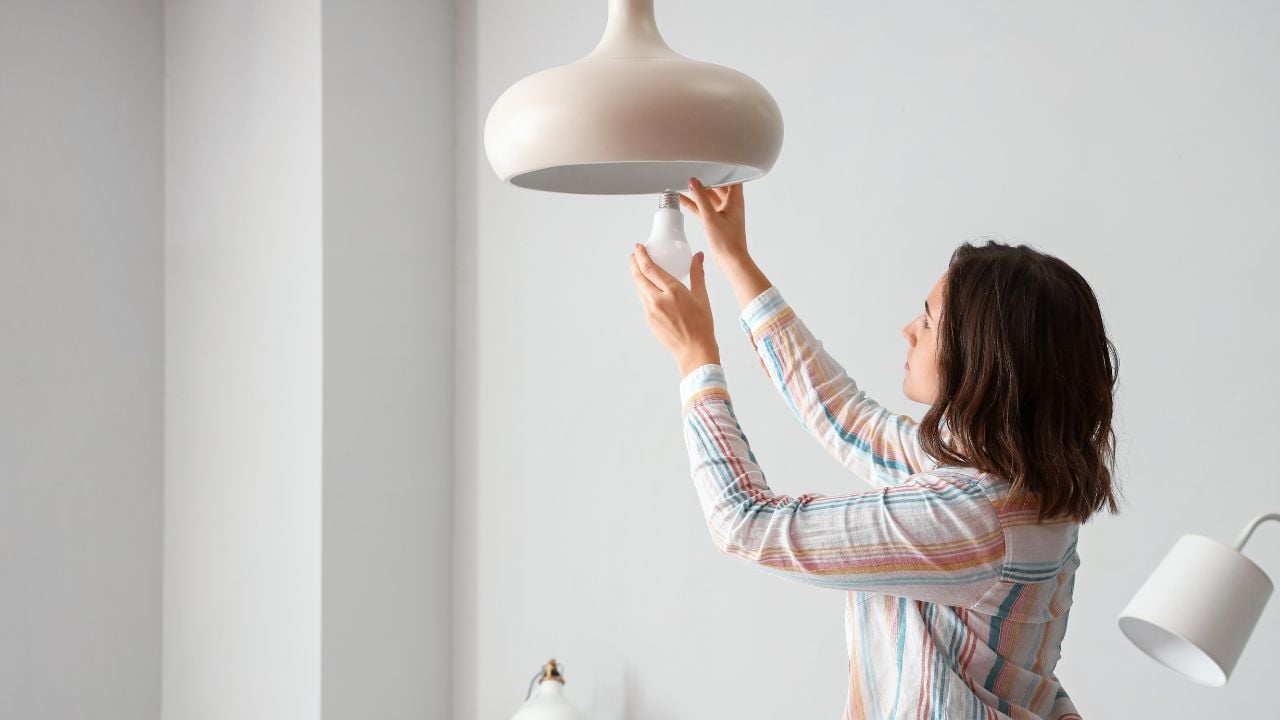 Woman changing light bulb in hanging lamp at home